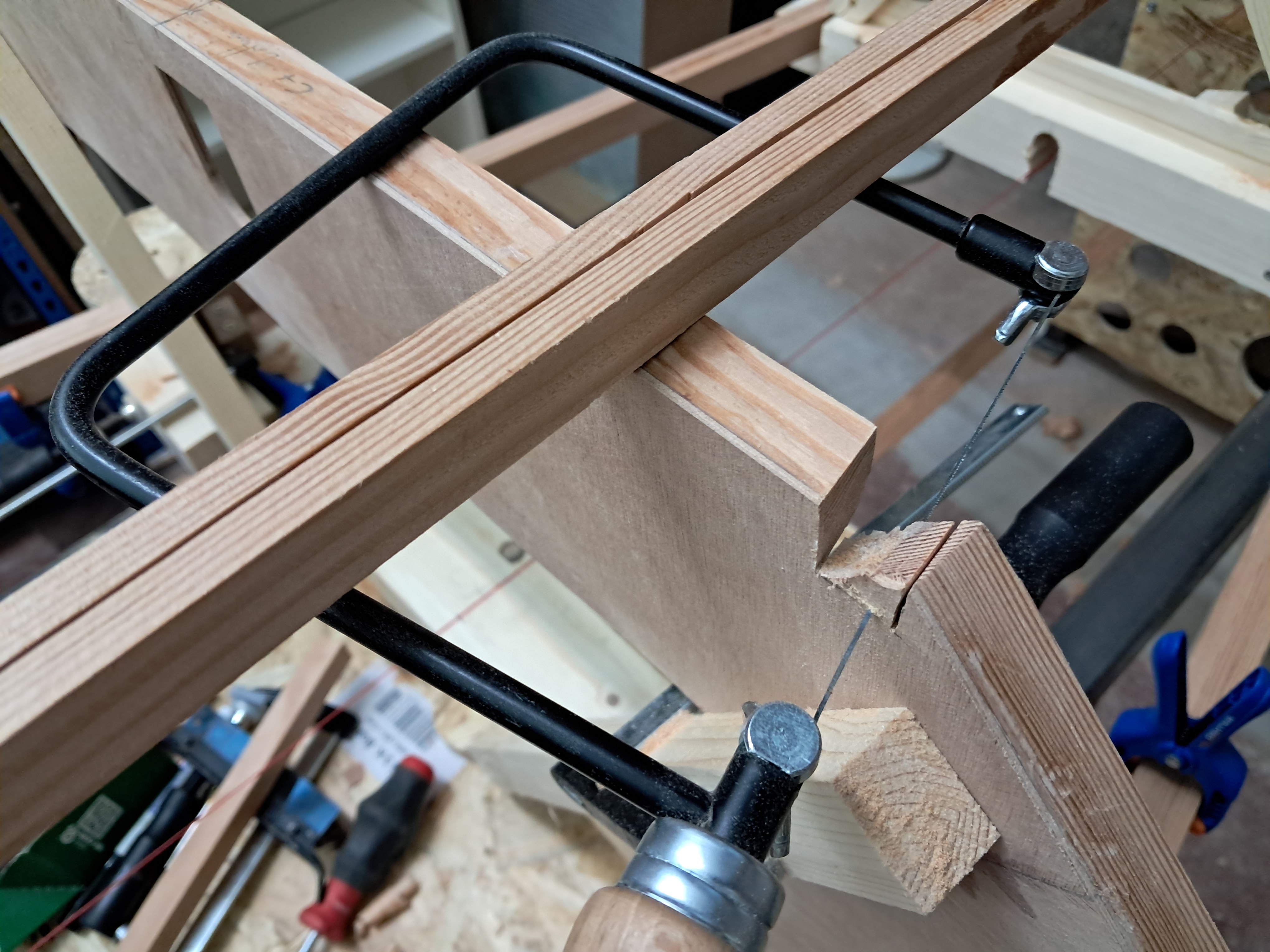 Using a coping saw to rough-cut a longeron notch in a bulkhead. The longeron sits in the partially opened notch while the floor is deepened incrementally.